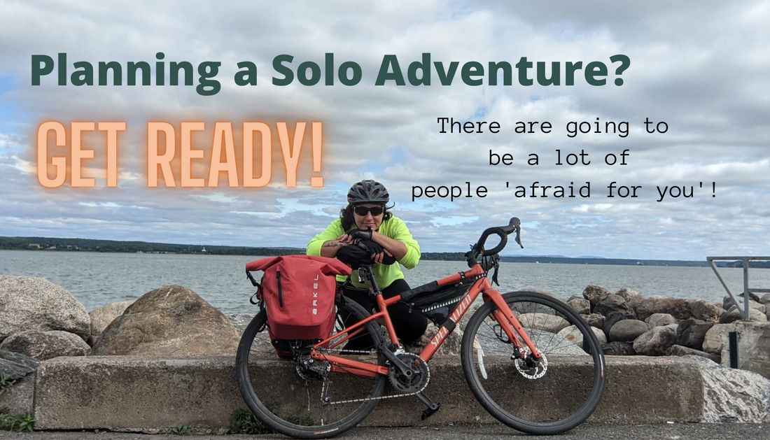 Image of woman with bicycle wearing a helmet in front of a shore line. Text across image: Planning a solo adventure? Get ready! There are going to be a lot of people "afraid for you"!