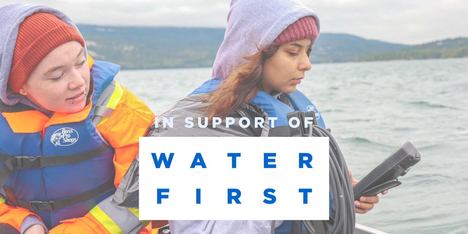 Image of two young women wearing life jackets on a boat on a lake. Holding water testing equipment. In Support of Water First logo over photo.