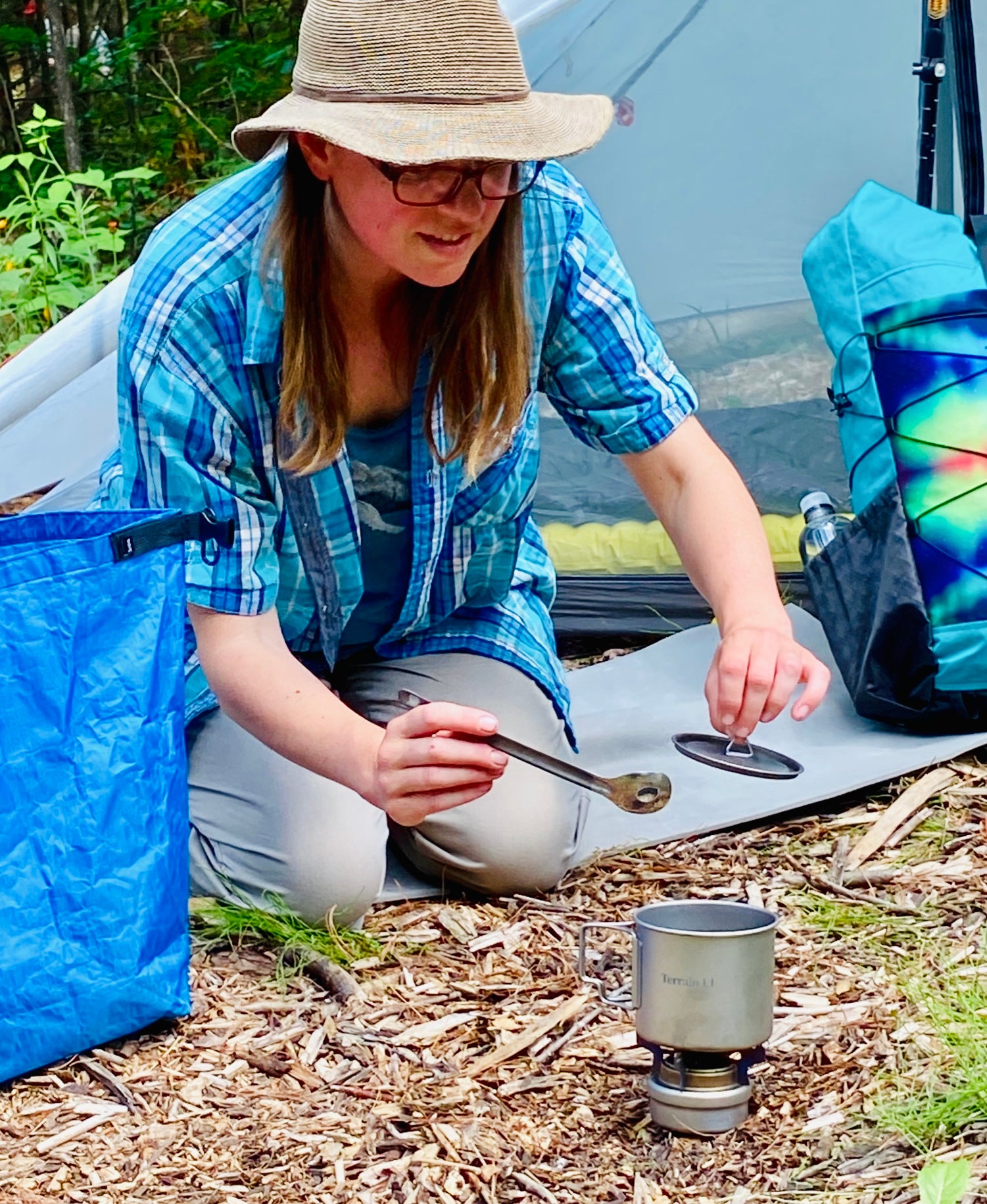 Woman camping lifting pot lid and holding spoon checking boiling pot on titanium alcohol stove