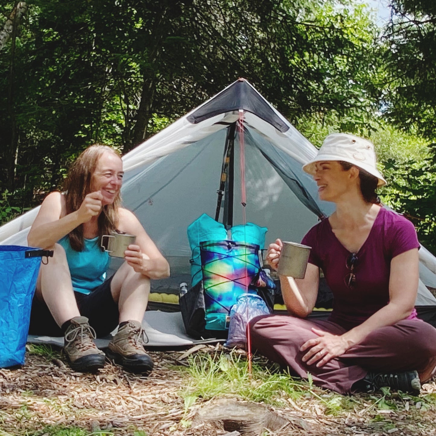 Two woman sitting in front of tent drinking/eating from titanium pots