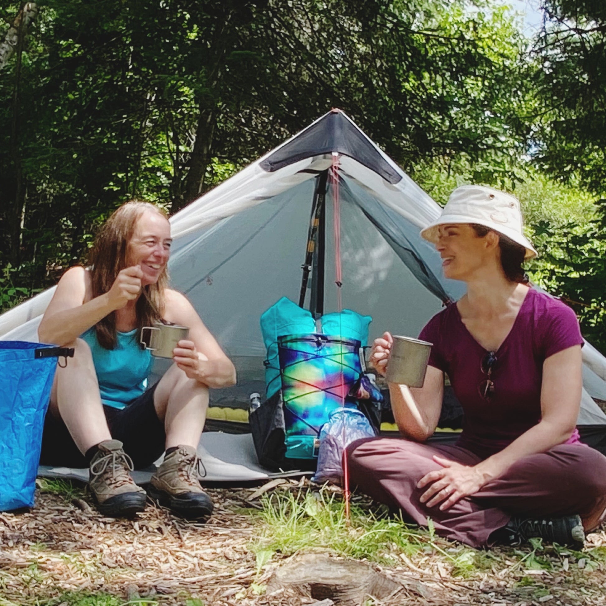 Two women sitting in front of tent drinking/eating out of titanium pots