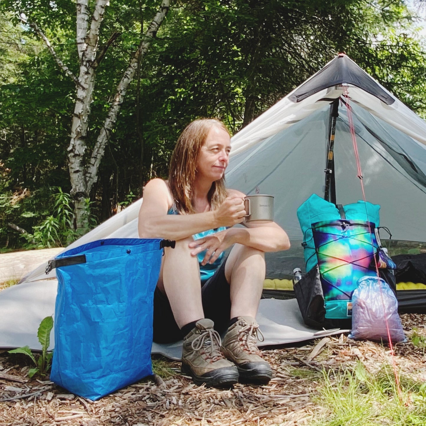 Woman sitting in front of tent holding/drinking from a titanium pot
